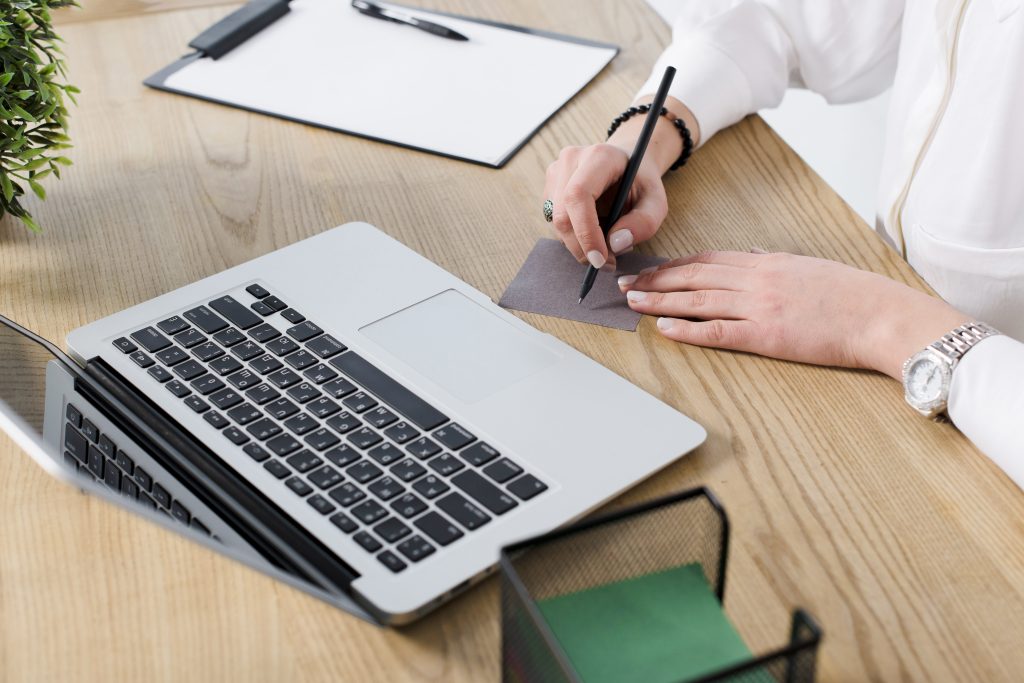 Young Businesswoman Writing Note With Pen Wooden Desk With Laptop 1024x683